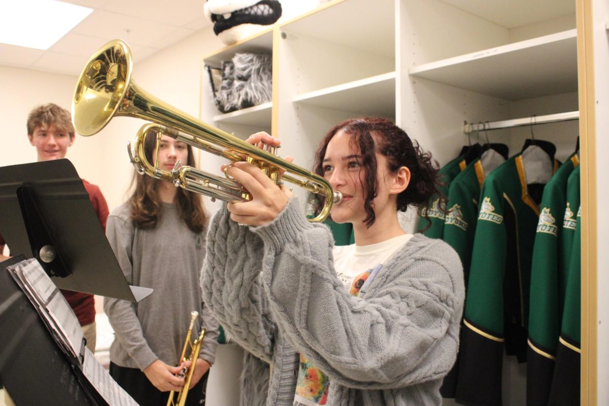 Green uniform, gold trumpet. Sophomore trumpet section leader Zaida Diaz Barcenas plays her trumpet alongside her upperclassmen trumpet section members in the band’s storage room. ” The brass section usually plays in a different room from woodwinds and percussion, we tend to overpower the band because we are so loud.” said junior Brayden Bowse.